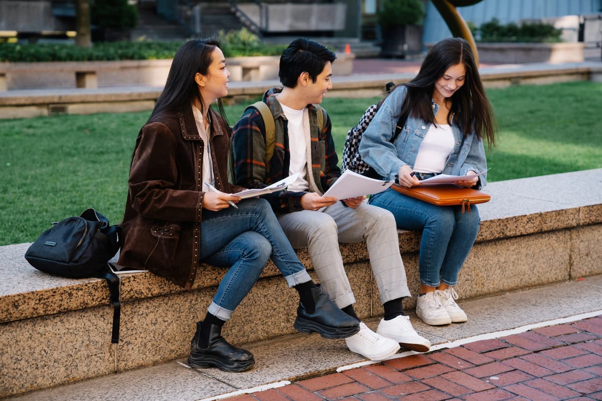 Three college students reviewing study materials together on a university campus