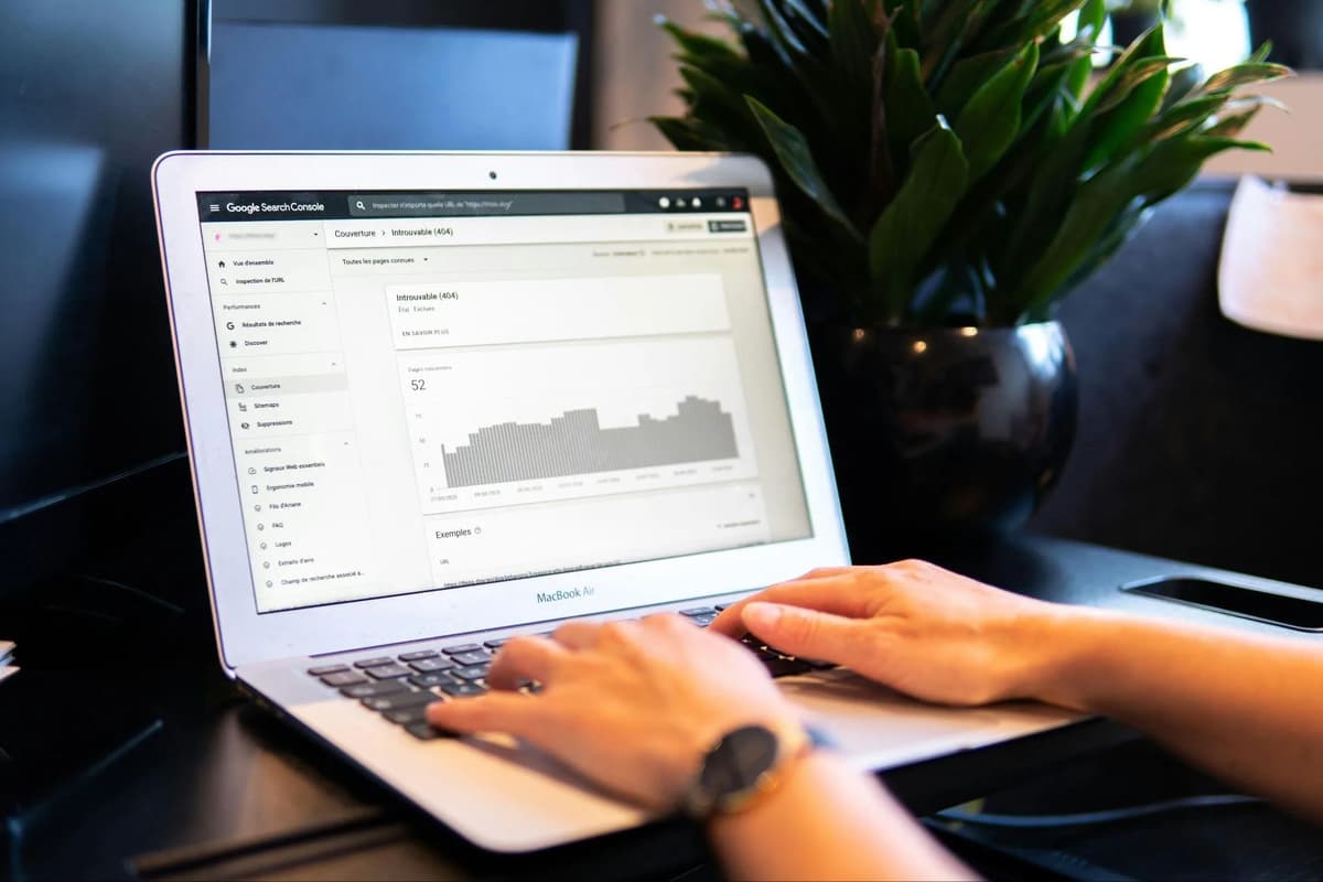 Person using a laptop displaying a Google Search Console report on 404 errors beside a potted plant.