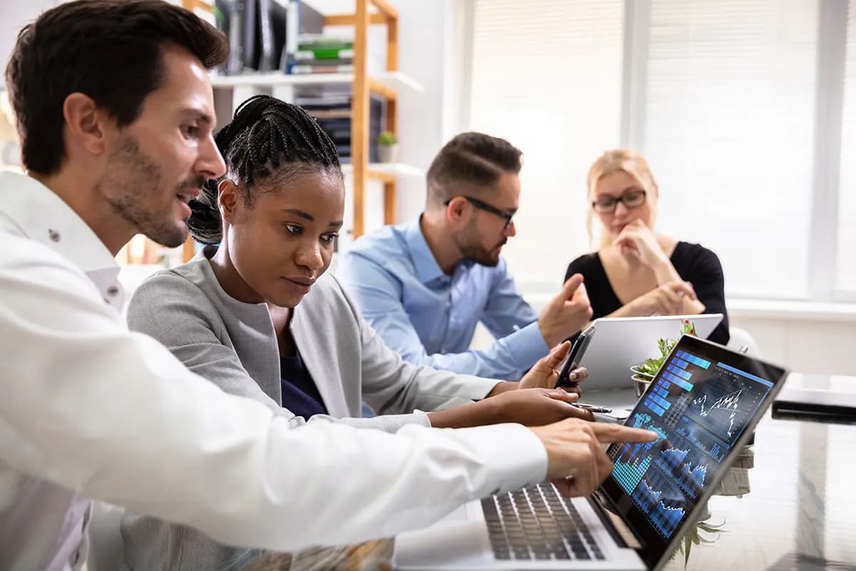 Diverse team of business professionals collaborating on data analysis using laptops and digital dashboards, illustrating Business Analytics in 2026, teamwork, data-driven strategy, and modern business intelligence in a professional office environment