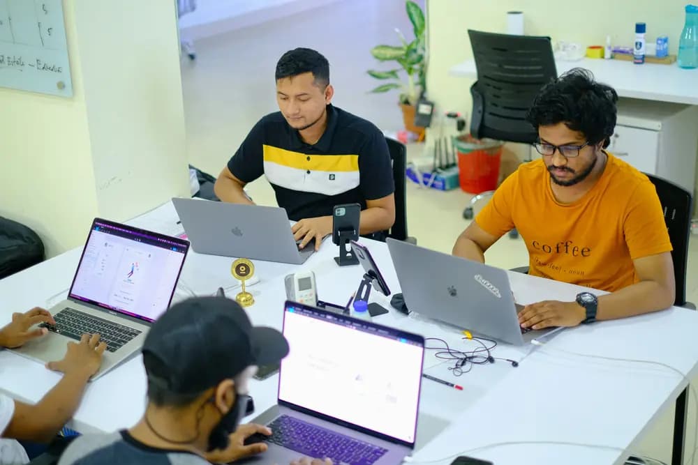Software engineers and developers working collaboratively on laptops in a modern office environment, coding, reviewing projects, and building software applications as part of a tech team.