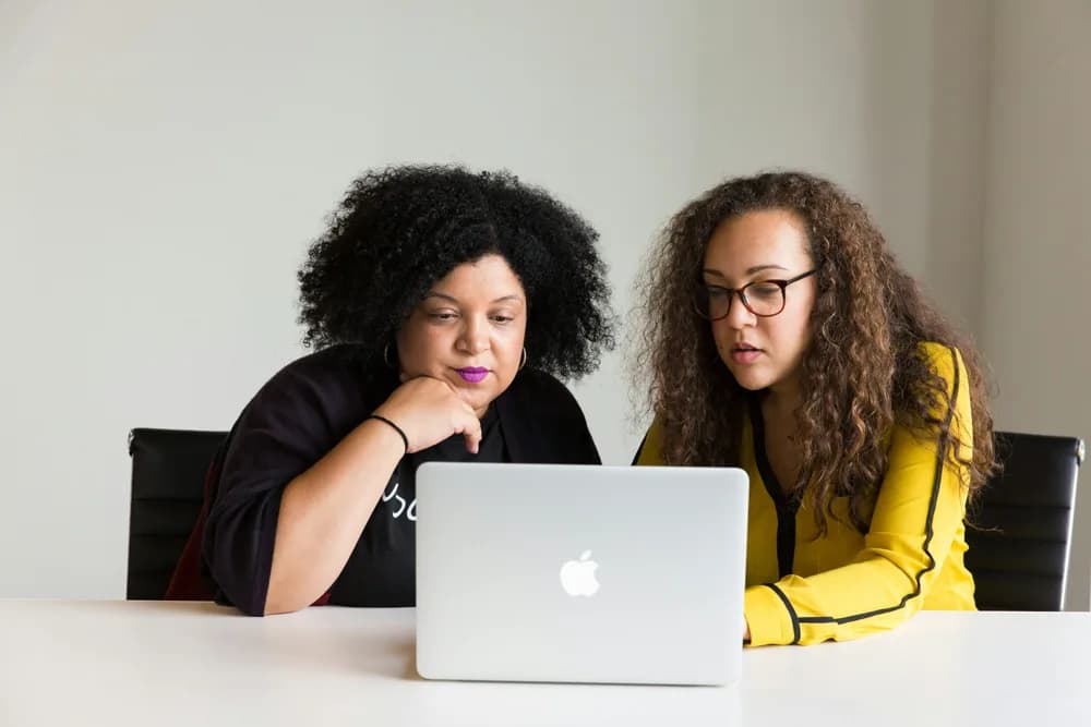 Two developers collaborating at a desk, reviewing code and discussing solutions on a laptop in a professional workspace.