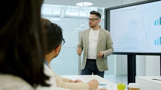 Man presenting data on a large screen to colleagues in an office meeting, representing the collaborative and dynamic nature of data analytics in 2026