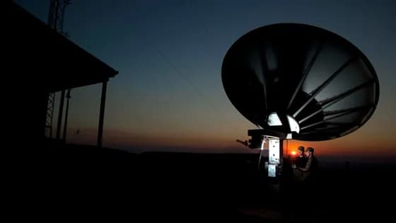 Two engineers adjusting a large satellite communications antenna. Satellite communications engineers often collaborate to ensure ground station equipment is optimized for clear signals. This role involves a blend of hands-on technical work and high-level network design to keep the world connected via space