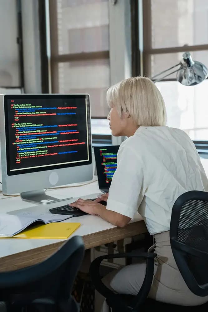 Full-stack developer working at a desk, writing and reviewing front-end and back-end code on a desktop computer to build modern web applications.