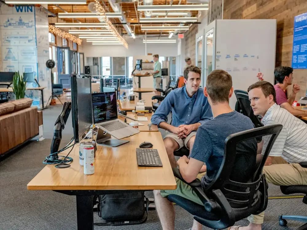 Software engineers collaborating in a modern open office, discussing code and development tasks at a shared workstation.