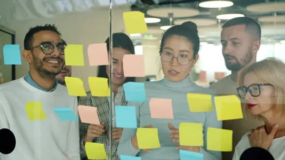 Diverse project management team brainstorming with sticky notes on glass wall in modern office Agile planning and collaboration trend for 2026