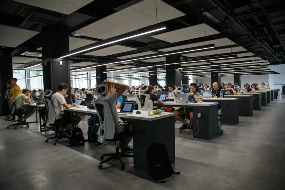 A large open-plan office filled with software engineers working on laptops at desks, collaborating and coding in a modern tech workspace.