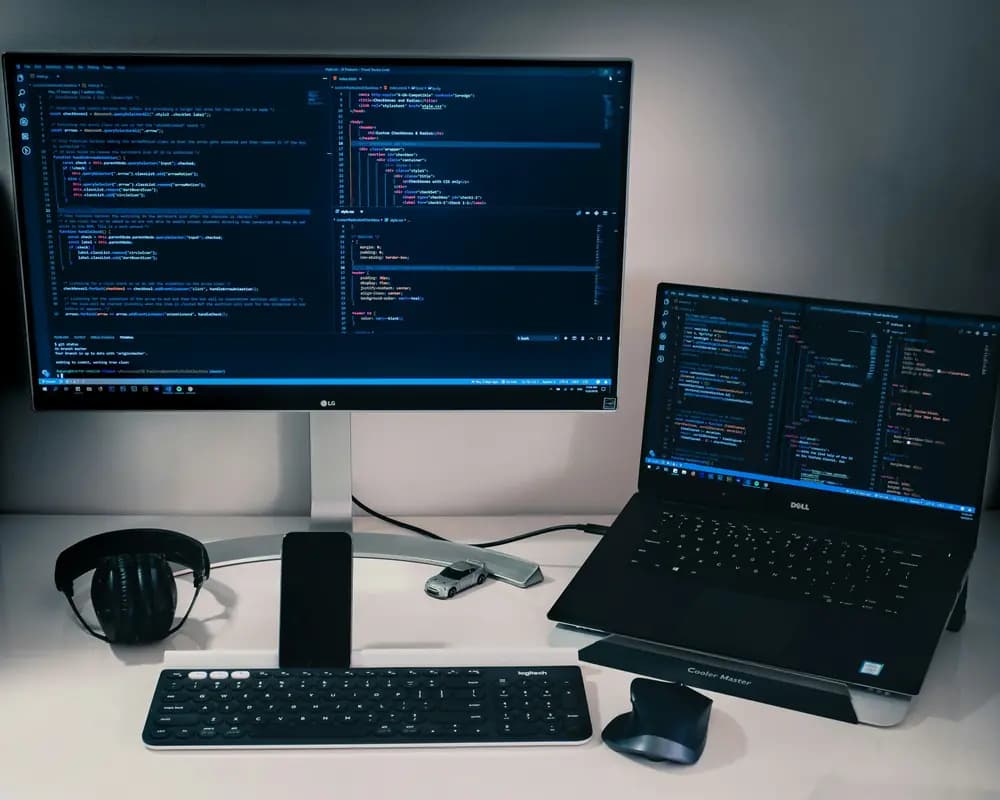 Software engineer workstation with laptop and external monitor displaying source code, showing a modern software development setup used for coding, debugging, and system engineering.