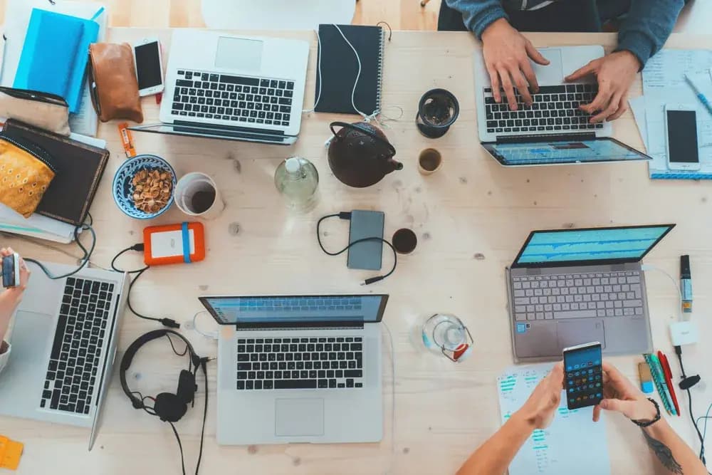 Top-down view of a collaborative workspace with multiple laptops, notebooks, and devices as professionals work, learn, and multitask together.