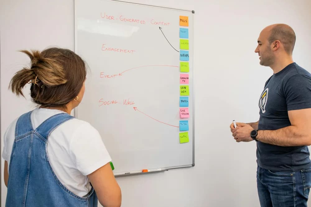 Two UX designers collaborate on a user journey flow at a whiteboard. In 2026, UI/UX design is a collaborative process blending creative brainstorming with data-driven insights.