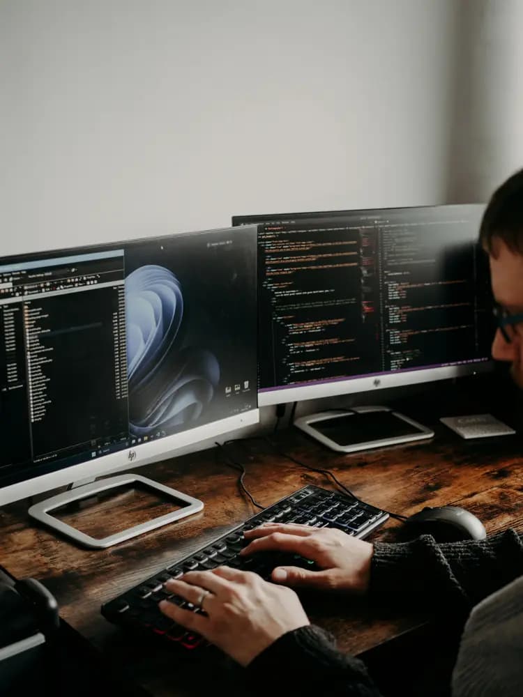 Cloud development engineer working on a multi-monitor workstation, writing and reviewing code used to build, deploy, and scale cloud-based applications.