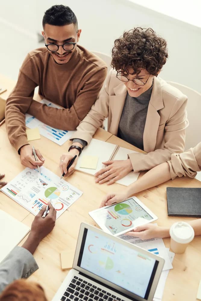 A diverse team collaborating at a table, reviewing charts and data visualizations on laptops and tablets during a business strategy meeting.